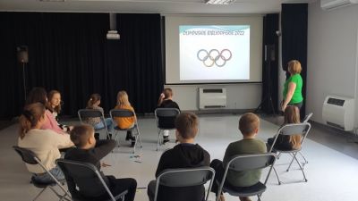 Dziesięcioro dzieci siedzących w okręgu, oglądają prezentację związaną z zimowymi dyscyplinami sportu